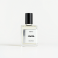 A clear glass perfume bottle with a black cap and a white label reading 'ISKRA' and 'VANDA vel L’apothicaire', centered on a clean off-white background.