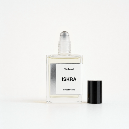 A clear glass perfume bottle labeled 'ISKRA' with a white label and a black cylindrical cap placed beside it on a clean white background.