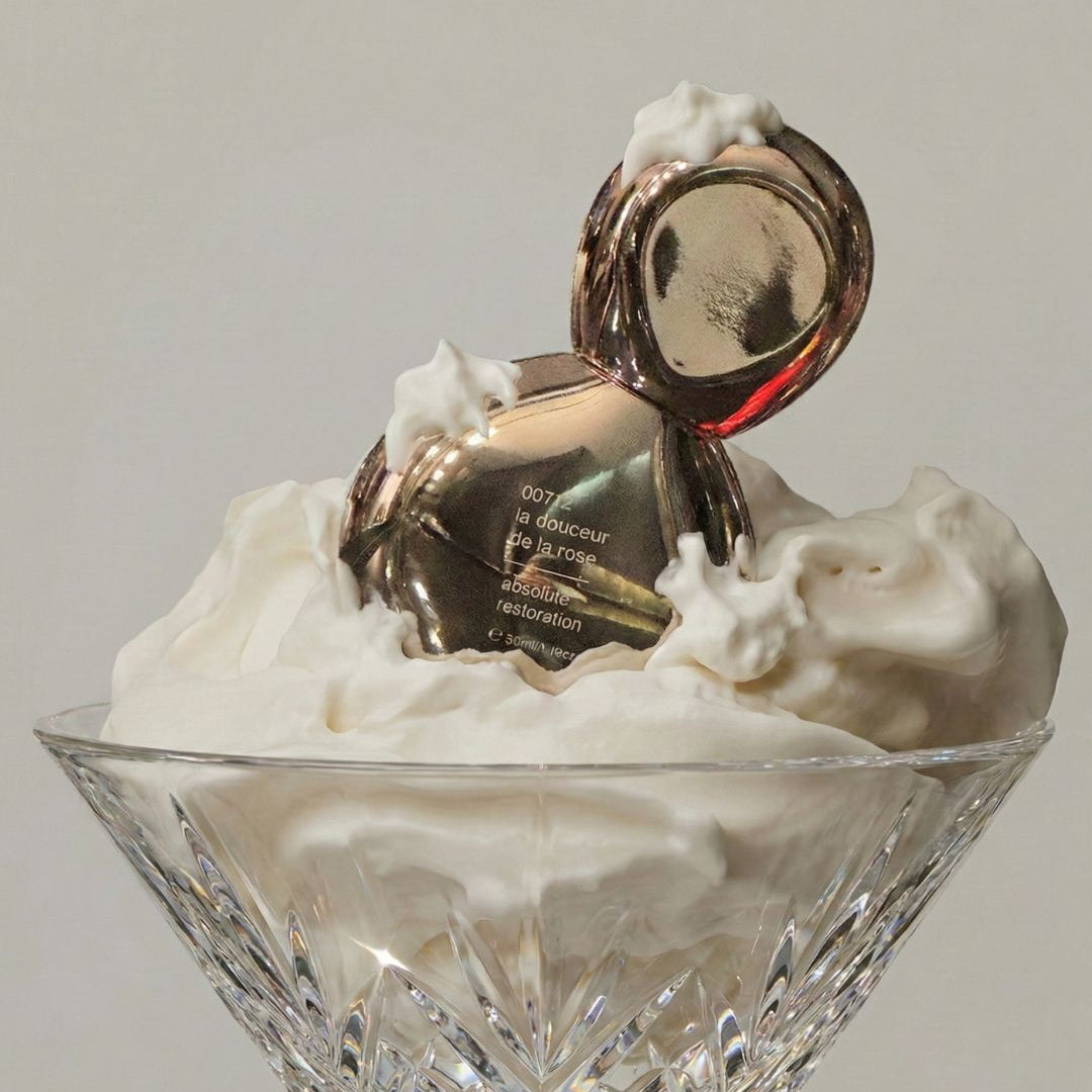 Crystal bowl with whipped cream and a small bottle of perfume on a light gray background